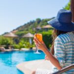 Mulher de chapéu segurando taça em espreguiçadeira em borda de piscina