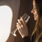 Mulher de fones de ouvido bebendo em taça no avião