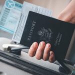 Pessoa segurando mala de viagem, passaporte e passagem